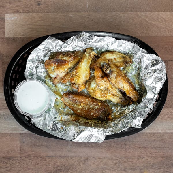 Seasoned fried chicken wings served in a foil-lined black basket with a cup of creamy dipping sauce.