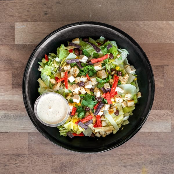 Overhead view of a chicken salad with lettuce, black beans, corn, peppers, tortilla strips, cilantro, and creamy dressing.