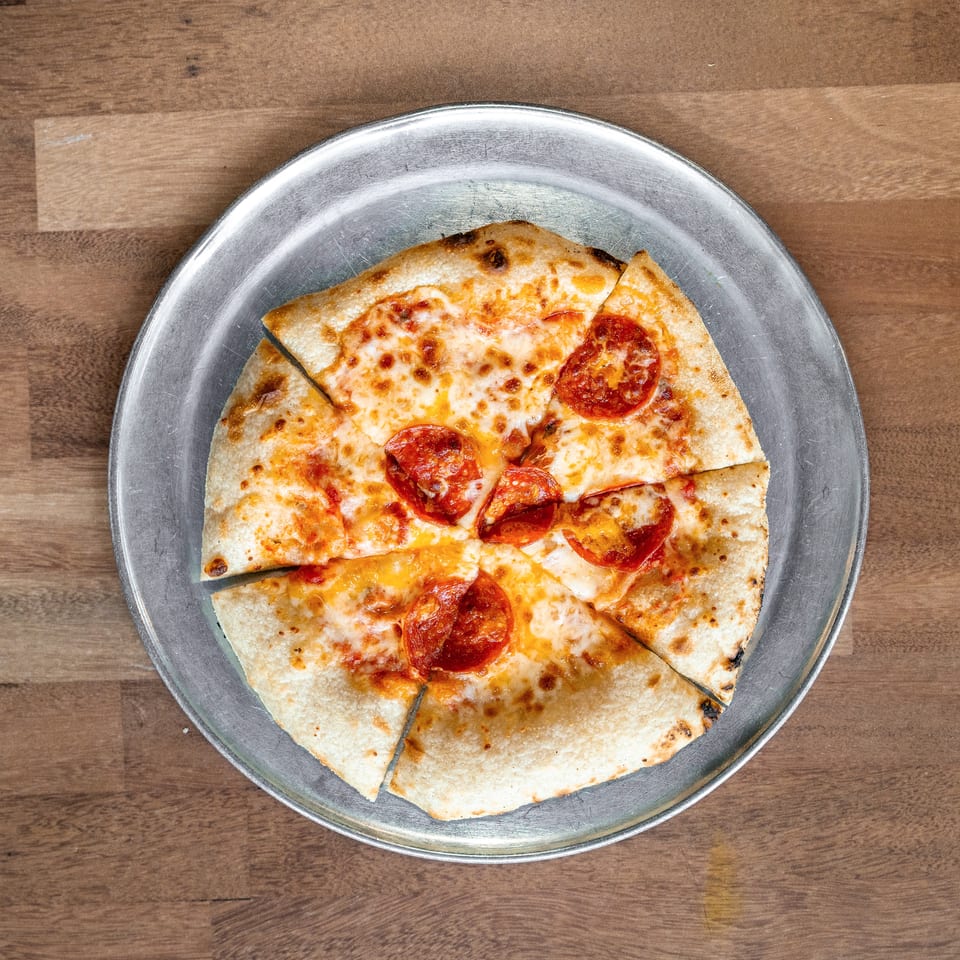Sliced pepperoni pizza with melted cheese on a metal plate atop a wooden table.