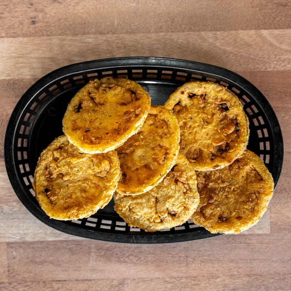 Basket of golden-brown fried vegetable fritters arranged on a wooden table.