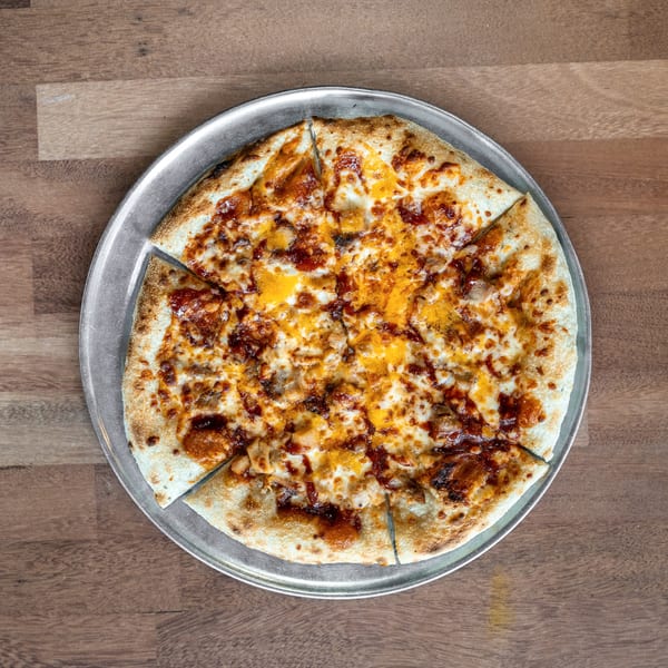 Cheesy meat-topped pizza cut into slices on a round metal tray atop a wooden table.
