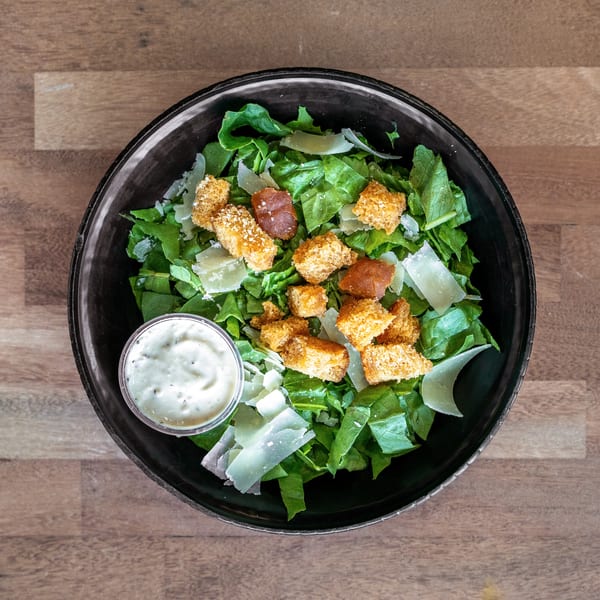 Top-down view of a Caesar salad with romaine lettuce, Parmesan shavings, crispy croutons, bacon, and creamy dressing.