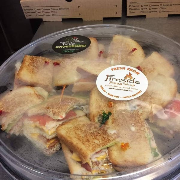 Tray of toasted sandwiches with assorted fillings under a clear cover, labeled Fresh from Fireside Pizza Shop.