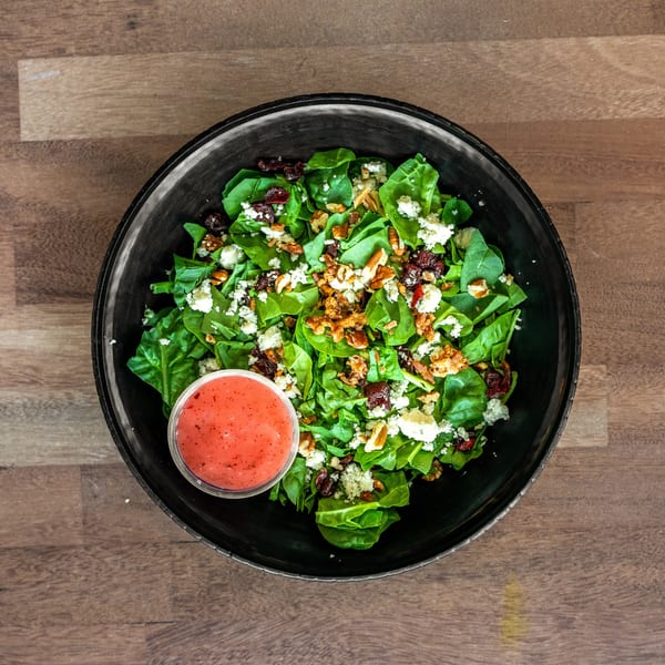 Overhead view of a spinach salad with cranberries, pecans, crumbled cheese, bacon, and pink dressing in a black bowl.