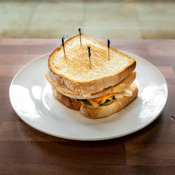 Stacked toasted sandwiches with cheese, greens, and creamy filling on a white plate, secured with cocktail picks.
