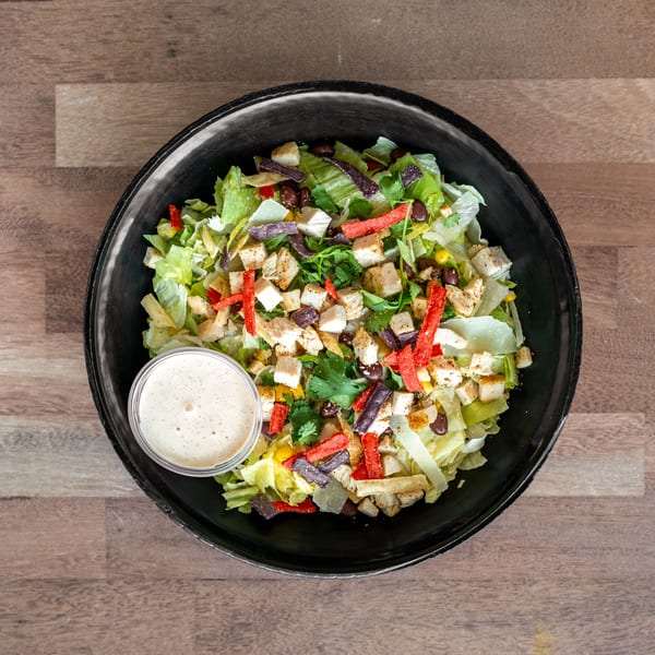 Overhead view of a chicken salad with lettuce, black beans, corn, tortilla strips, cilantro, and creamy dressing in a black bowl.